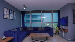 Un salón moderno con un sofá azul, una mesa de centro de madera y un amplio ventanal con vistas a la ciudad.