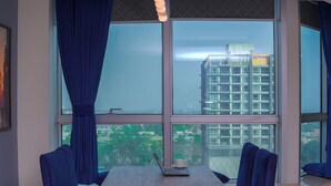 Una habitación moderna con un ventanal grande, una mesa con sillas y vistas a un paisaje urbano.