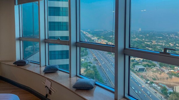 Habitación de hotel con ventanas amplias que ofrecen vistas a una autopista y edificios circundantes.