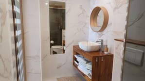 Une salle de bain moderne avec un sol en marbre, un meuble-lavabo en bois doté d’un grand évier, un miroir et un espace douche.