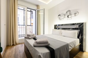 Habitación de hotel con cama, ventana con cortinas, balcón y una obra de arte en la pared.