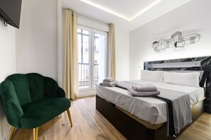 Un dormitorio con una cama, una silla verde, una ventana con cortinas y una obra de arte colgada en la pared.