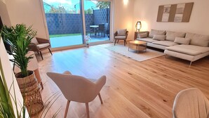 Ein großzügiges Wohnzimmer mit einem großen Schiebeglastür, die auf eine Terrasse führt, einem Sofa, einem Sessel und einer Lampe.