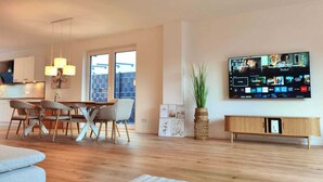 Ein modernes Wohnzimmer mit Essbereich, einem an der Wand befestigten Fernseher und Blick ins Freie.