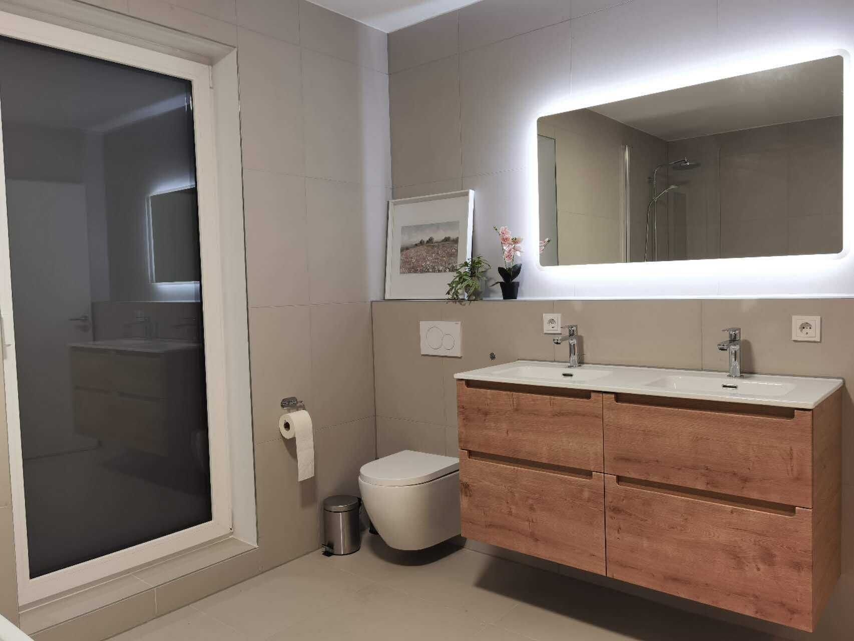 A modern bathroom with a large mirror, a sink, and a toilet.