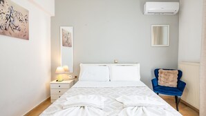 Ein Hotelzimmer mit Bett, Nachttisch, Lampe, Klimaanlage, Sessel und Bildern an den Wänden.