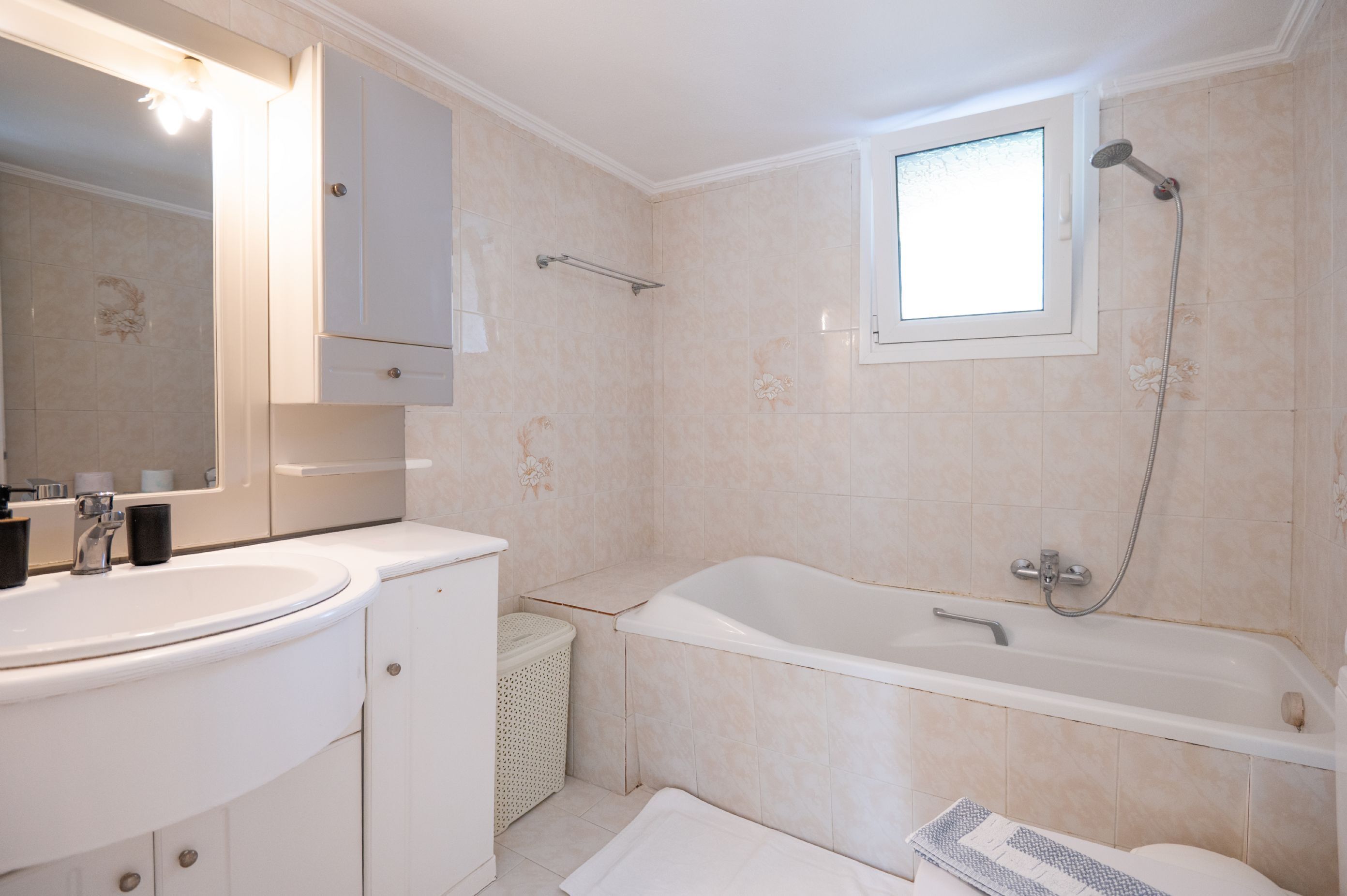 A bathroom with a white sink, a bathtub, and a window.