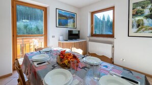 A dining area with a table set for four, a television on a small table, and large windows with scenic views. - The Space🏔 Beautiful Mountain House 5 Minutes from the Alleghe Slopes – Comfort & Nature in the Heart of the DolomitesExperience a unique stay in the Dolomites in a mountain house cared for in every detail, perfect for ski lovers in winter and hikin (Alleghe)
