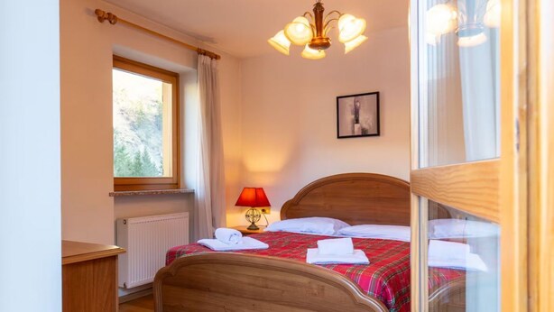 A bedroom with a wooden bed, a window with curtains, a radiator, and a wall-mounted picture. - The Space🏔 Beautiful Mountain House 5 Minutes from the Alleghe Slopes – Comfort & Nature in the Heart of the DolomitesExperience a unique stay in the Dolomites in a mountain house cared for in every detail, perfect for ski lovers in winter and hikin (Alleghe)