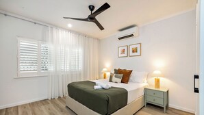 A neatly arranged bedroom with a bed, bedside lamps, a nightstand, and a ceiling fan. - Family-Friendly Pool & Patio Retreat, Walk to Beach & Dining (Trinity Beach)