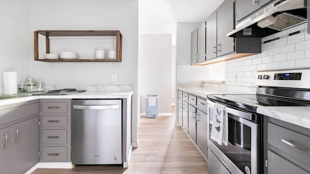 A modern kitchen with grey cabinets, a built-in dishwasher, a stainless steel oven, and a white tiled backsplash. - 🏆FSU Condo - King bed, great for Orientation & campus tours (Tallahassee)