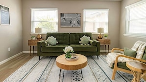 A living room with a green sofa, two side tables with lamps, a coffee table, and a patterned rug. - 🏆FSU Condo - King bed, great for Orientation & campus tours (Tallahassee)