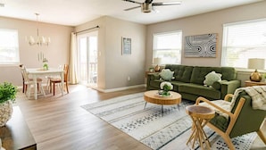 A spacious living room with a dining area, a green sofa, a ceiling fan, and a patterned rug. - 🏆FSU Condo - King bed, great for Orientation & campus tours (Tallahassee)