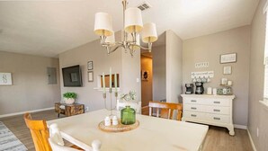 A dining area with a wooden table, chairs, a chandelier, and a white dresser with a coffee station. - 🏆FSU Condo - King bed, great for Orientation & campus tours (Tallahassee)