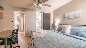 A bedroom with a bed, a desk, a chair, a ceiling fan, and a door leading to a bathroom. - 🏆FSU Condo - King bed, great for Orientation & campus tours (Tallahassee)