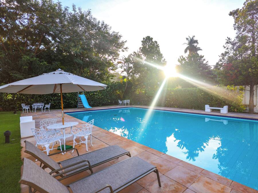 A swimming pool with lounge chairs and a table, surrounded by greenery.