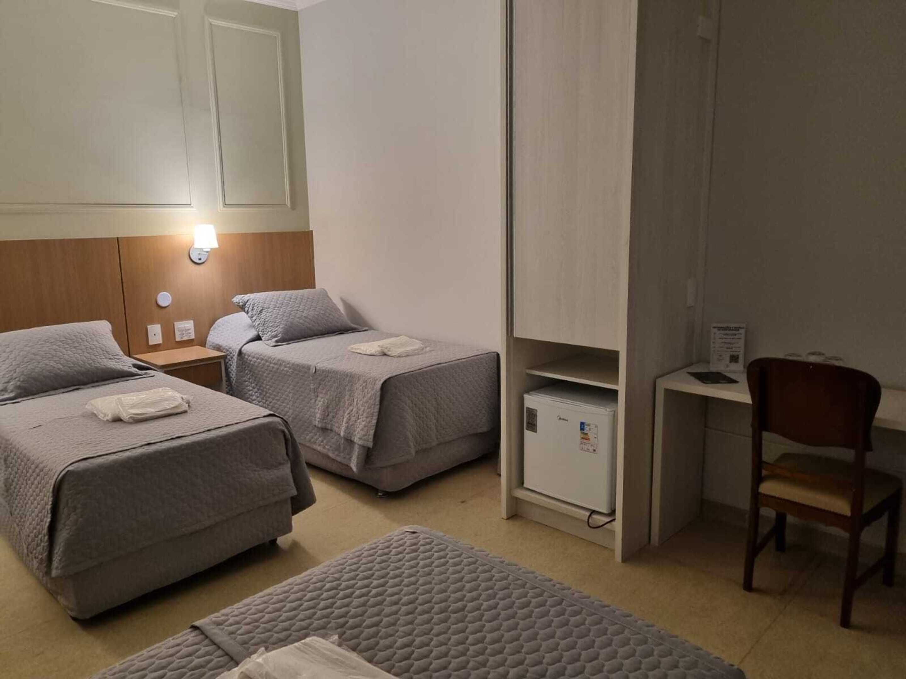 A room with two beds, a desk, a chair, and a small refrigerator.