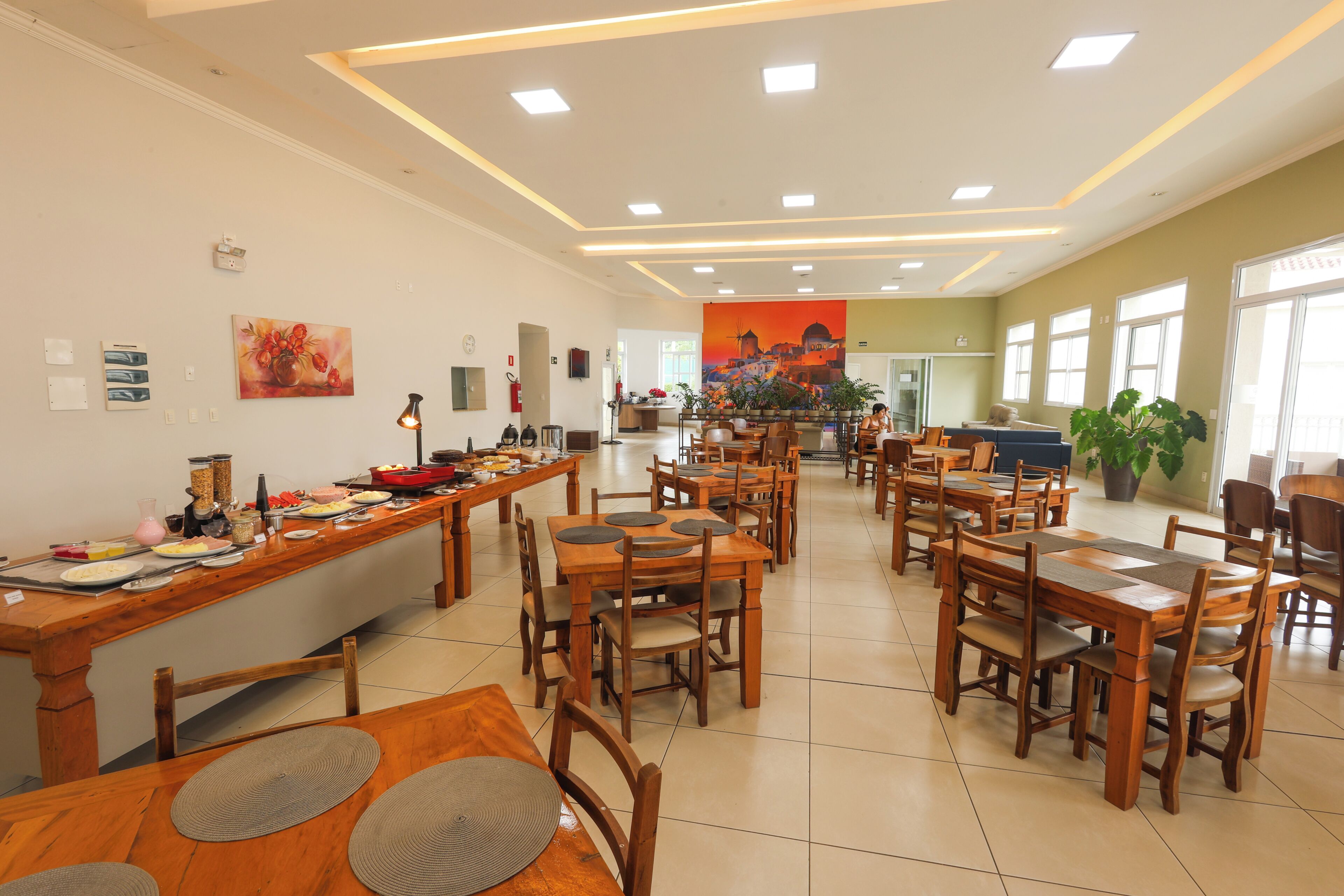 A spacious dining area with multiple wooden tables and chairs, a central buffet table, and a large mural on the back wall.