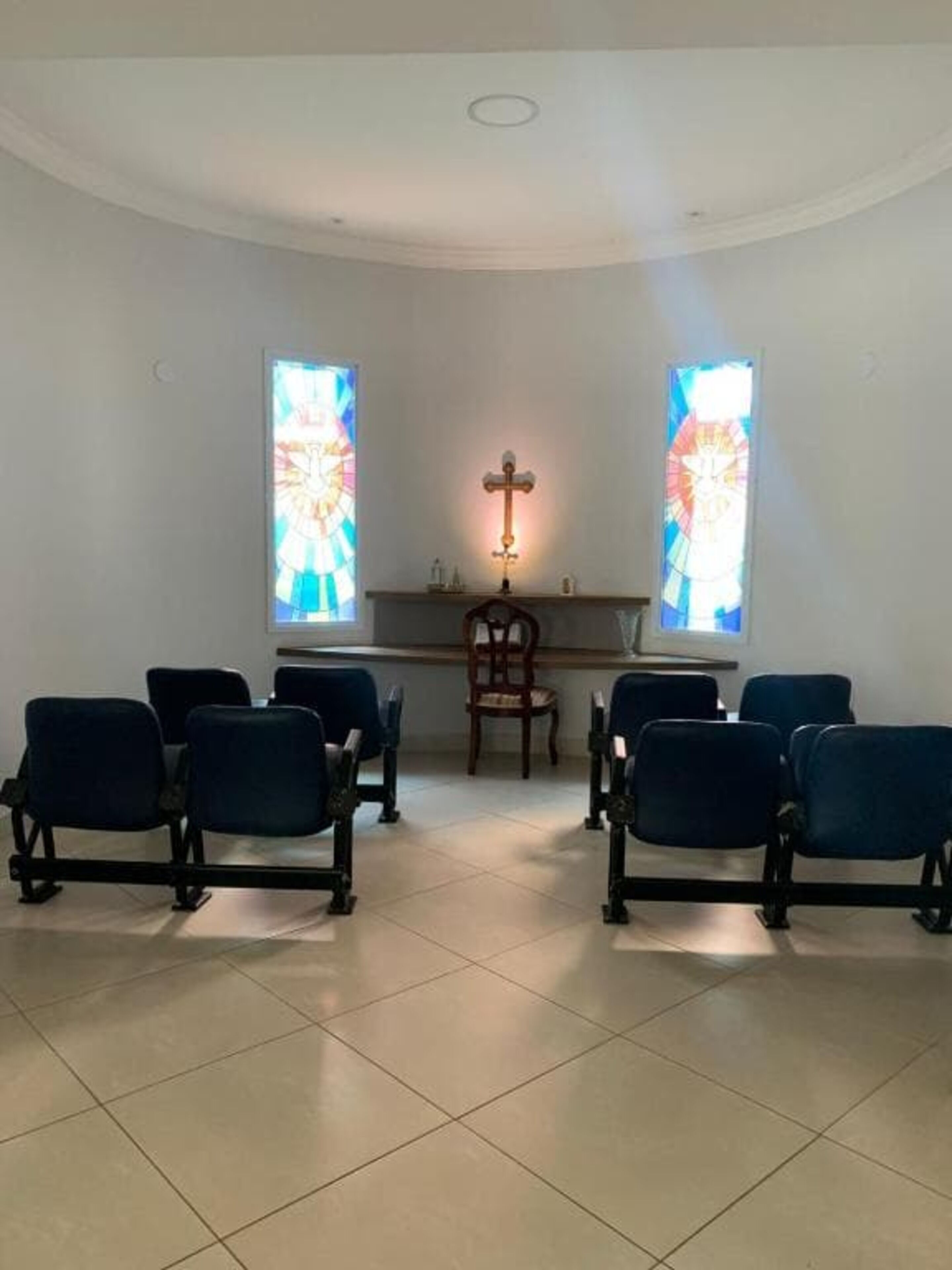A church interior with pews, a wooden chair, and two stained glass windows.