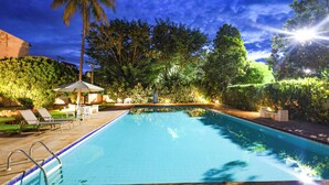 A swimming pool with lounge chairs and umbrellas, surrounded by greenery and trees.