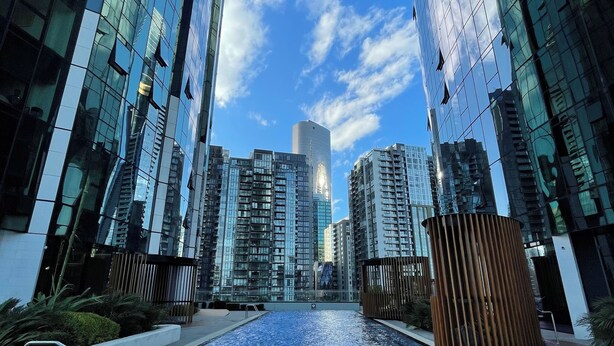 Un edificio moderno con fachada de vidrio reflectante, una piscina central y cielo despejado.