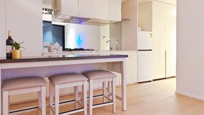 Una cocina moderna con armarios blancos, una isla central con taburetes de bar, una estufa a gas y un refrigerador.