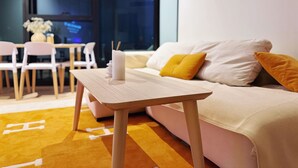 Una sala de estar moderna con una mesa de madera, un sofá con cojines amarillos y blancos, y un comedor con sillas y un jarrón de flores.