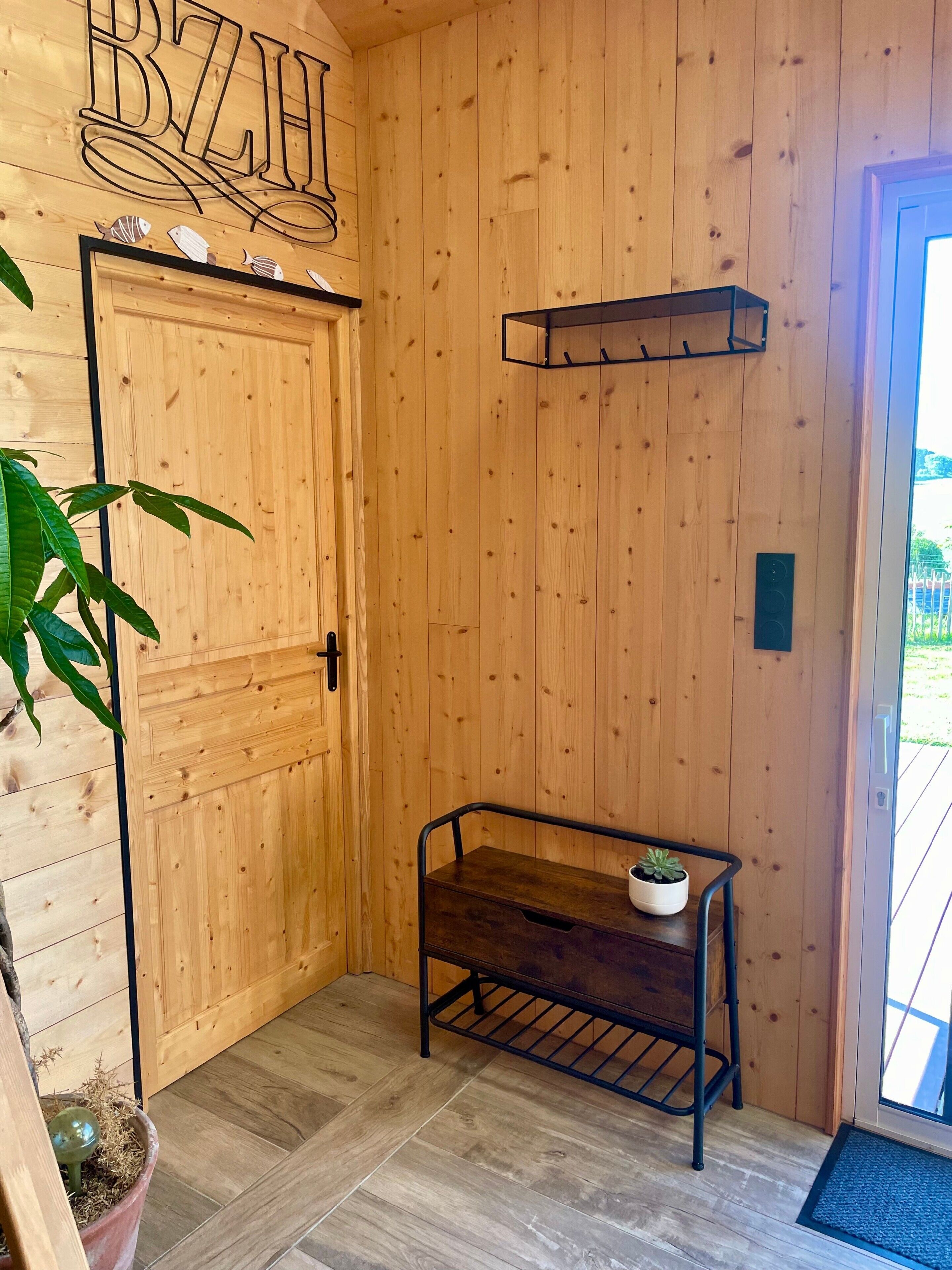 Un interior de fusta amb una porta, un banc metàl·lic amb una planta i una paret de fusta decorada amb un peix.