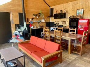 A cozy cabin interior with a wooden interior, a dining area with a red sofa, a kitchen with modern appliances, and a fireplace. - Breton Chalet with Nordic Bath and Golf Views in Plouarzel (Plouarzel)