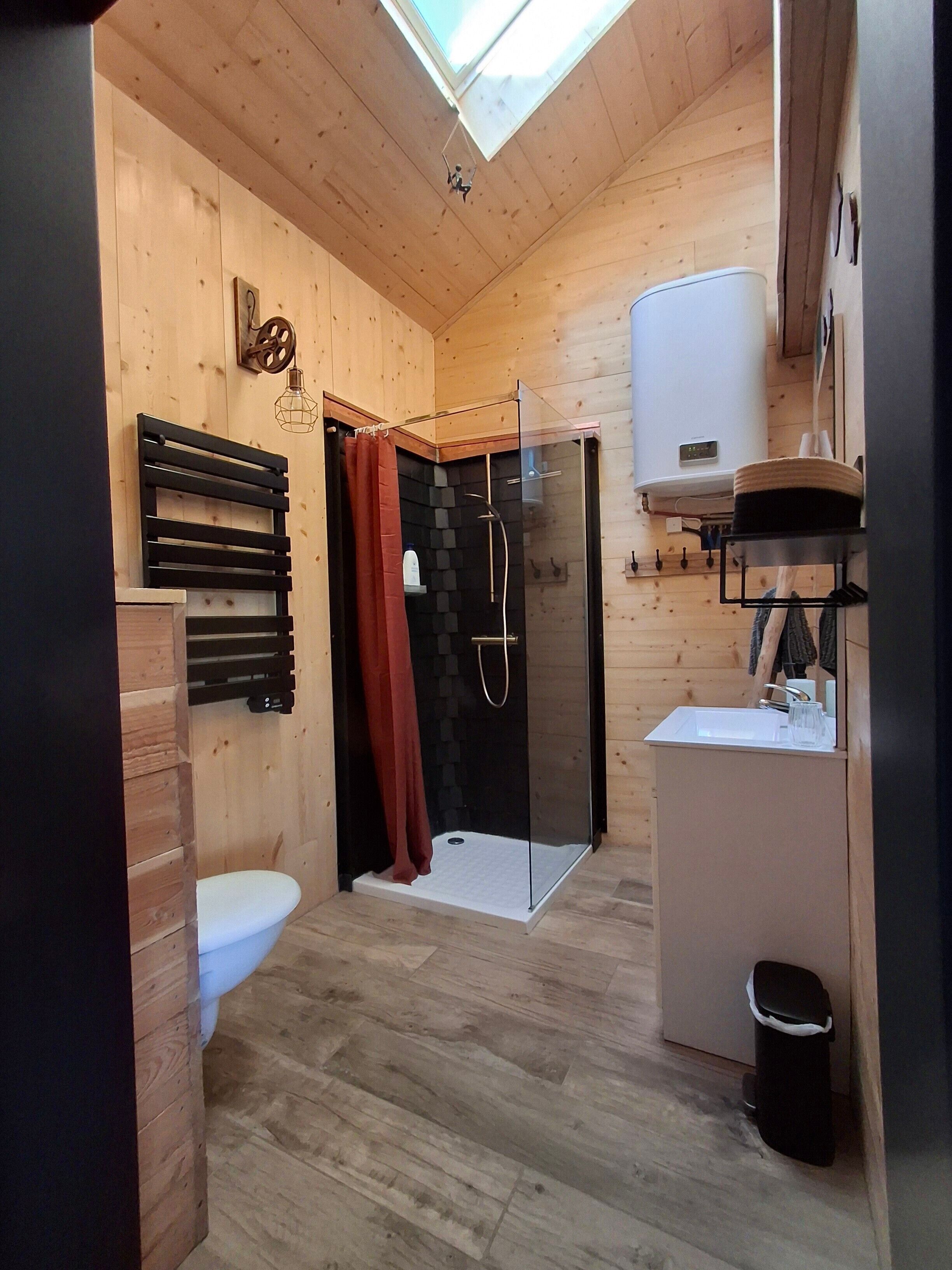 En lille træhytte med ovenlys, brusebad, toilet og håndvask.