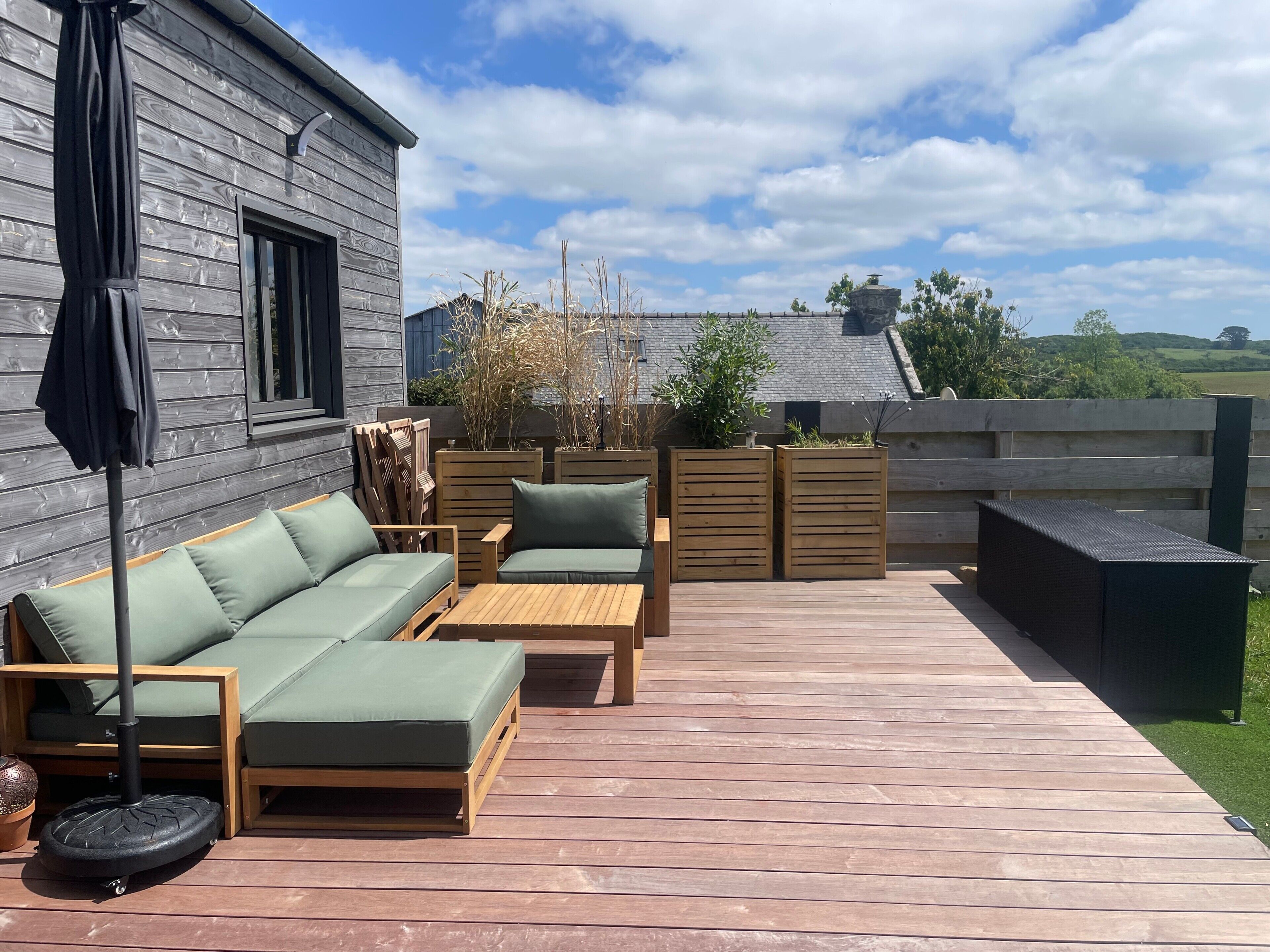 En træterrasse med sofa, stole og bord, omgivet af et træhegn og planter.
