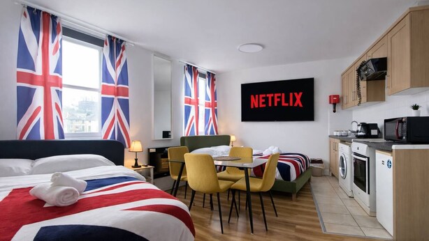 Ein Hotelzimmer mit Bett, Schreibtisch, Stuhl, Tisch, einer Waschmaschine und einer Küchenzeile.
