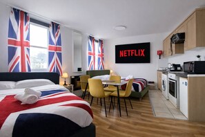Une chambre d’hôtel équipée d’un lit, d’un bureau, d’une chaise, d’une table, d’une machine à laver et d’un coin cuisine.