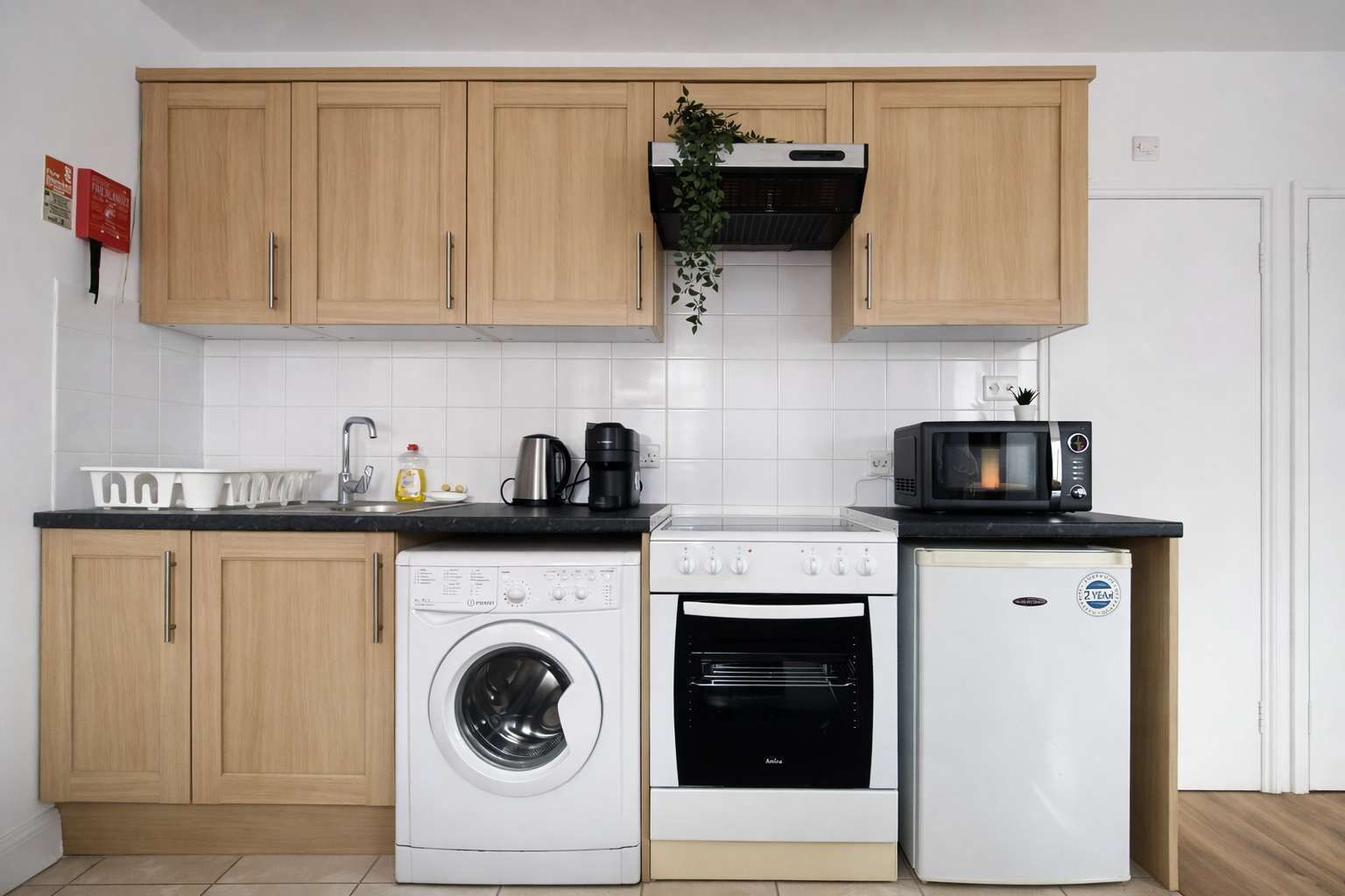 Eine kompakte Küche mit Holzausstattung, einer Waschmaschine, einem Backofen, einer Mikrowelle und einem kleinen Kühlschrank.