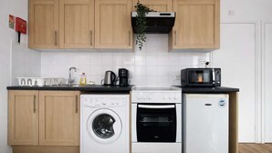 Eine kompakte Küche mit Holzausstattung, einer Waschmaschine, einem Backofen, einer Mikrowelle und einem kleinen Kühlschrank.