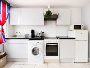 Una cucina moderna con mobili bianchi, una lavatrice, un forno, un microonde e un piccolo frigorifero.