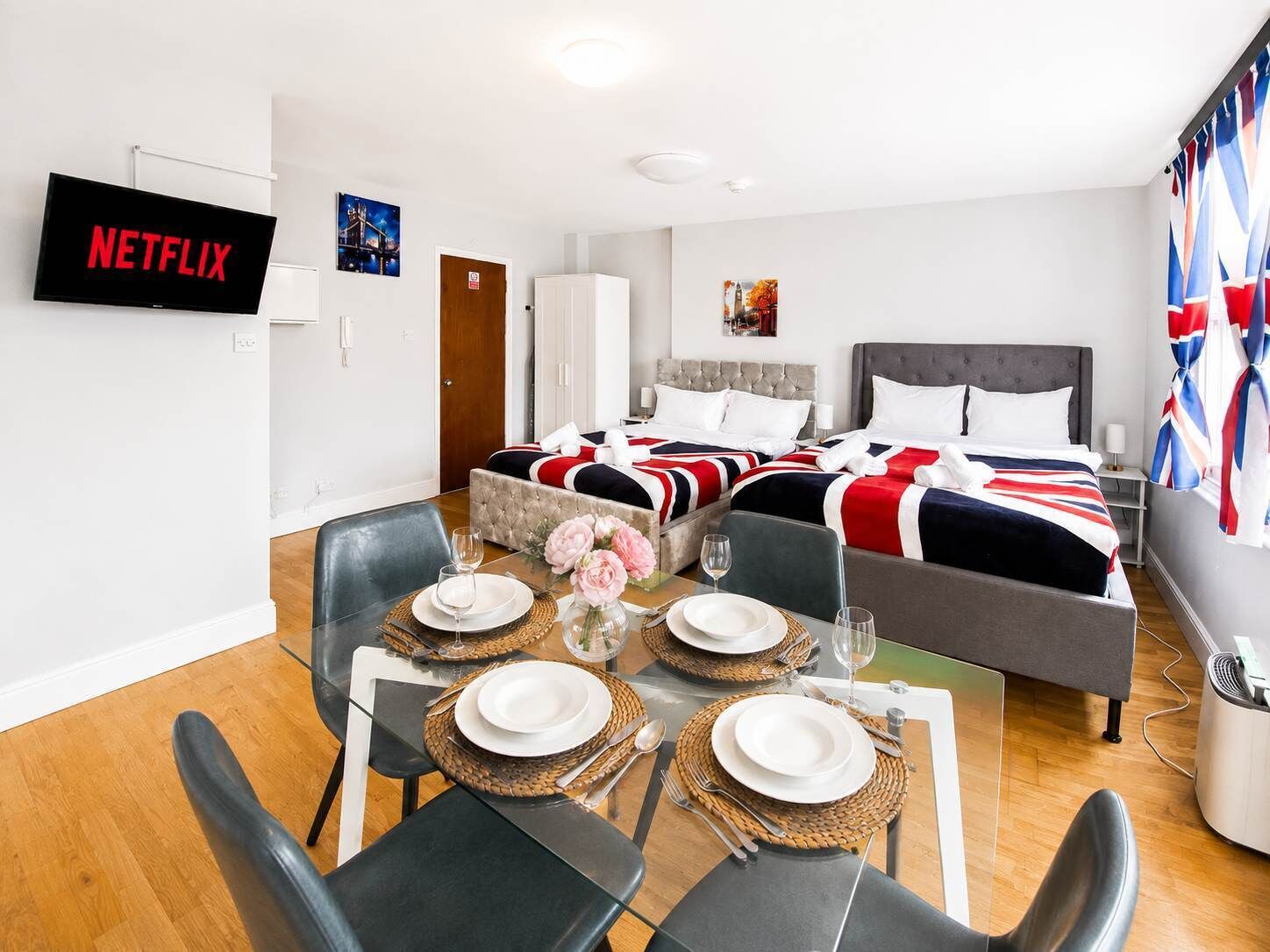 Una camera d'albergo con angolo ristoro, due letti con lenzuola rosse, bianche e blu, una televisione e un quadro appeso al muro.