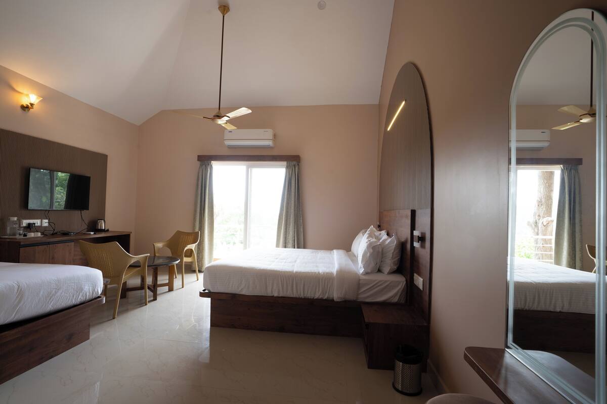 Habitación de hotel con dos camas, un escritorio, sillas, un espejo grande y un equipo de aire acondicionado.