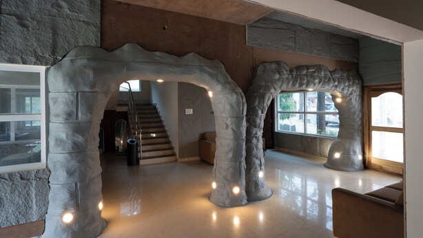 A modern interior with a stone archway leading to a staircase, a large window, and a seating area. - MSB Silver Spring Resort Private Limited (Yelagiri)