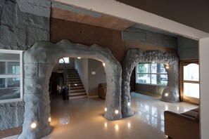 A modern interior with a stone archway leading to a staircase, a large window, and a seating area. - MSB Silver Spring Resort Private Limited (Yelagiri)