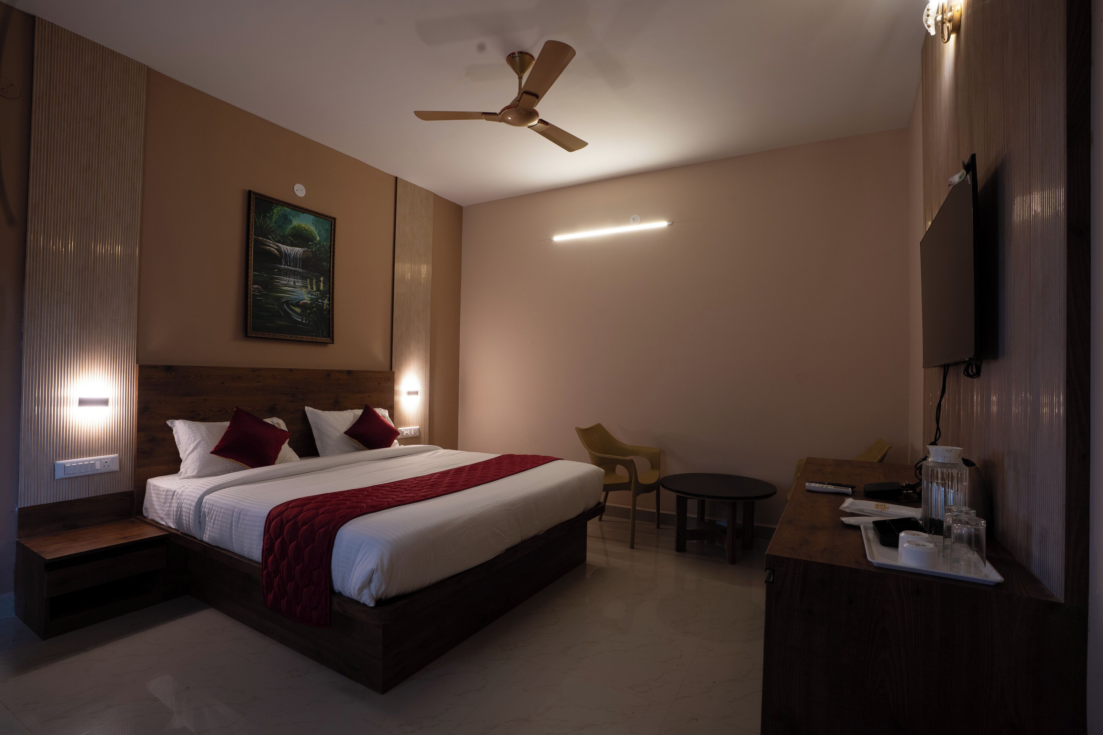 A hotel room with a bed, a desk, a chair, a television, and a ceiling fan.
