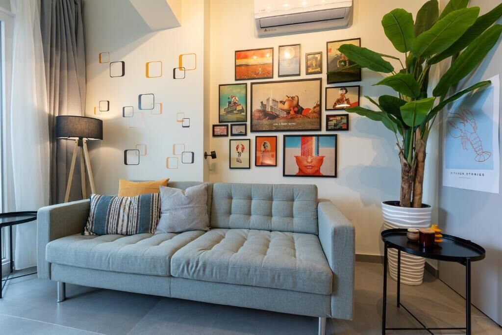 Un salón moderno con un sofá gris, una lámpara de pie y una planta grande en maceta.