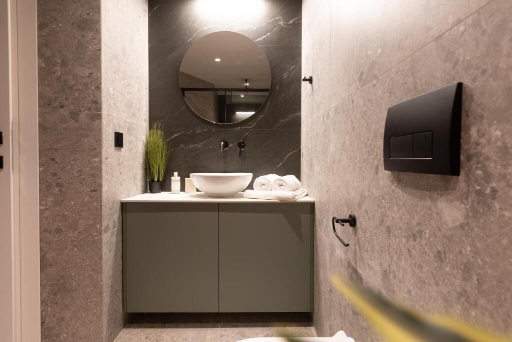 A modern bathroom with a marble wall, a round mirror, a sink with a bowl, and a towel rack.