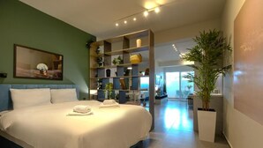 A modern hotel room with a large bed, a built-in bookshelf, a dining area, and a potted plant. - The Next Chapter Nilie Hospitality MGMT (Thessaloniki)