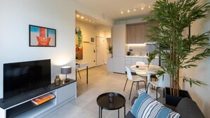 A modern living room with a flat-screen TV, a sofa, and a dining area with a table and chairs. - The Next Chapter Nilie Hospitality MGMT (Thessaloniki)