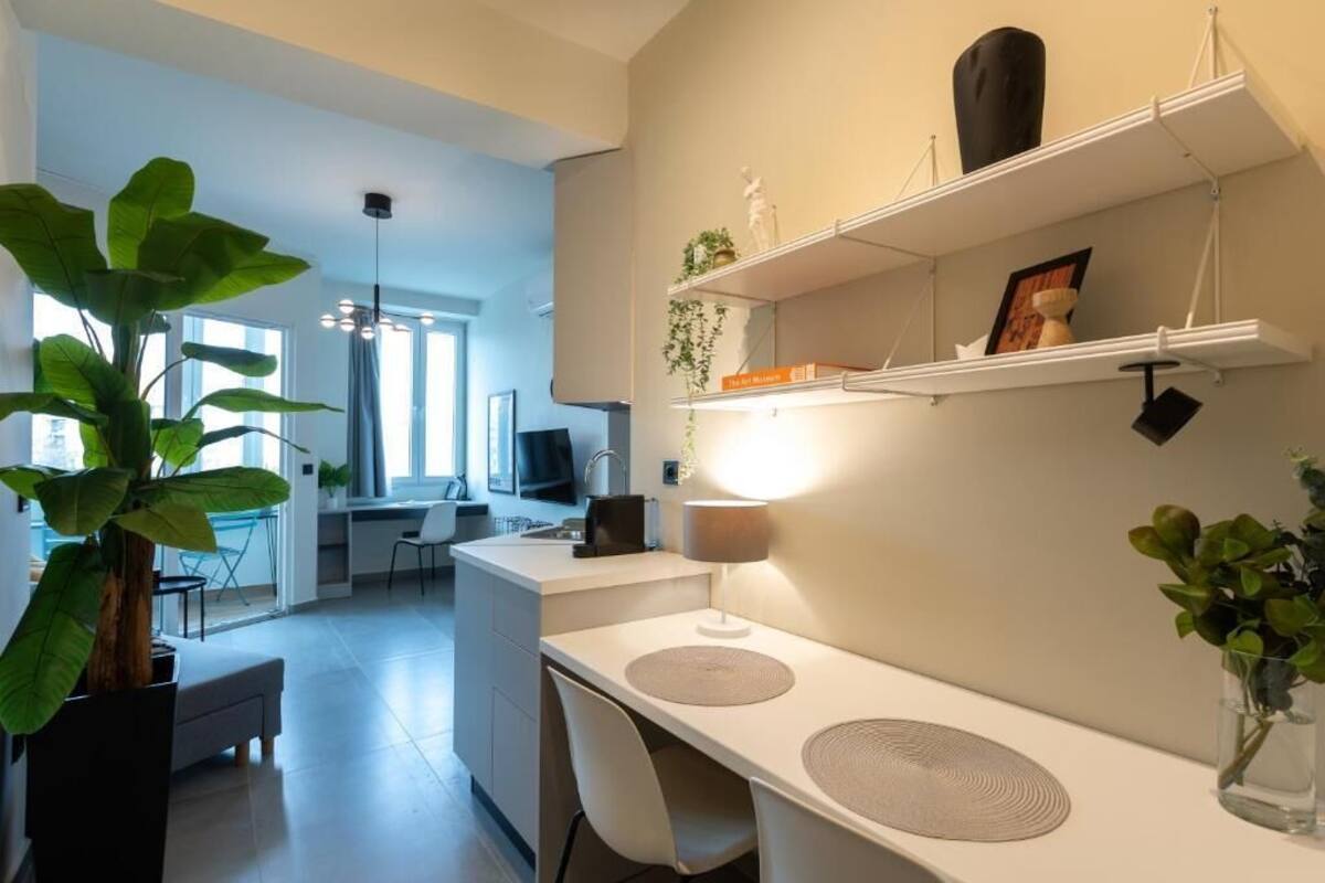 Una cucina moderna con mobili bianchi, un'area pranzo con tavolo e sedie, e un'ampia pianta in vaso.