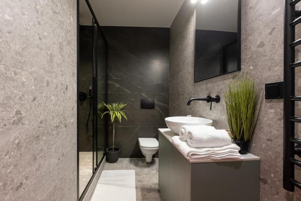 Ein modernes Badezimmer mit einer Duschkabine aus Glas, einer weißen Toilette, einem großen Waschbecken mit Spiegel und zwei Topfpflanzen.