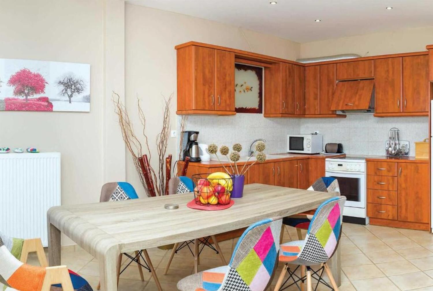 A modern kitchen with wooden cabinets, a dining table with colorful chairs, and a white refrigerator.