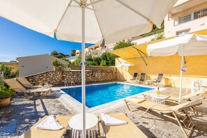 A pool area with lounge chairs, umbrellas, and a stone wall. - Villa Cleo Beach in Mparmpati (Corfu)
