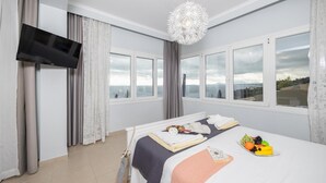 Een hotelkamer met een bed, een aan de muur bevestigde televisie en grote ramen met uitzicht op zee.